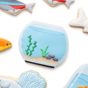 May include: Assortment of fish-themed cookies, including a fishbowl with aquatic plants and several fish cookies. The fish cookies feature various designs, including a neon tetra with red and blue stripes, and a betta fish with a detailed tail.
