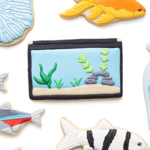 May include: Assortment of decorated sugar cookies in the shape of aquatic life. Includes a goldfish, a fish tank with plants, and various fish designs. The cookies are decorated with bright colors and intricate details, perfect for an ocean-themed event.