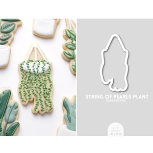 May include: A cookie cutter in the shape of a string of pearls plant. The cutter is white and is shown next to a decorated cookie of the same shape. The text "STRING OF PEARLS PLANT COOKIE CUTTER" is below the cutter.