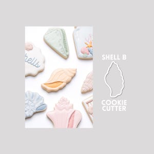 May include: A collection of decorated sugar cookies shaped like various seashells in pastel colors including pink, blue, and peach, alongside a white outline of a shell labeled SHELL B COOKIE CUTTER. The cookies feature intricate icing details.