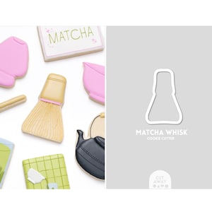 Puede incluir: Imagen de galletas con temática de matcha y un cortador de galletas. Las galletas incluyen un batidor, un cuenco de matcha y un letrero que dice "Matcha". El cortador de galletas es blanco y tiene forma de batidor de matcha.