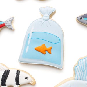 May include: Assortment of fish-shaped cookies, including a goldfish, a fish in a bag, and other colorful fish designs. The cookies are decorated with orange, yellow, blue, black, and white icing. A fun treat for an aquatic-themed party.