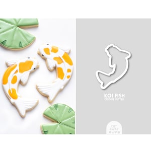 May include: Two white and orange koi fish cookies with black spots, and two green leaf cookies. A white outline of a koi fish cookie cutter is shown on a gray background with the text "KOI FISH COOKIE CUTTER".