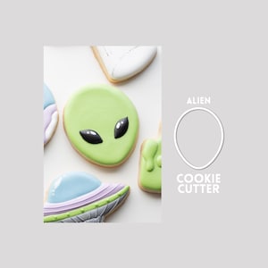 Könnte beinhalten: Eine Sammlung verzierter Kekse mit einem Alien-Kopf mit schwarzen Augen, einer fliegenden Untertasse und anderen Formen, neben einer weißen Umrisszeichnung eines Alien-Ausstechers mit dem Text ALIEN COOKIE CUTTER in weißen Buchstaben.