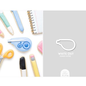 May include: A white plastic cookie cutter shaped like a correction tape dispenser, labeled "WHITE OUT COOKIE CUTTER" in white text on a gray background, alongside various school supply-shaped cookies including pens, scissors, and a notebook.