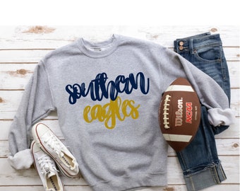 May include: A gray sweatshirt with the words "Southern Eagles" in blue and gold lettering. A football, a pair of white sneakers, and blue jeans are also pictured.