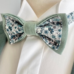 Puede incluir: Una pajarita verde claro con un estampado floral en blanco, azul y marrón. La pajarita se coloca sobre una camisa blanca con cuello y una blazer verde claro. Los bordes de la pajarita son de color verde claro liso.