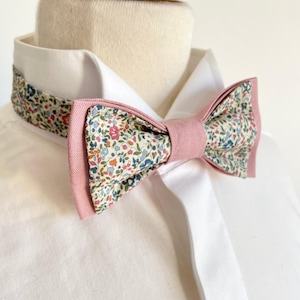 Peut inclure: Un nœud papillon rose et blanc avec un motif floral. Le nœud papillon est en tissu et a un dos rose.