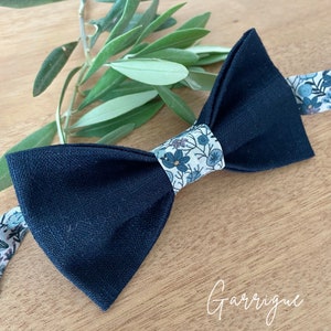 Può includere: Un papillon nero con un motivo floreale bianco e blu sul davanti. Il papillon è realizzato in tessuto di lino.