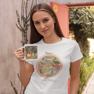 May include: White t-shirt with a nature-themed illustration of a forest scene with mushrooms, animals, and a feather. The text "NATURE MAMA" is printed below the illustration.
