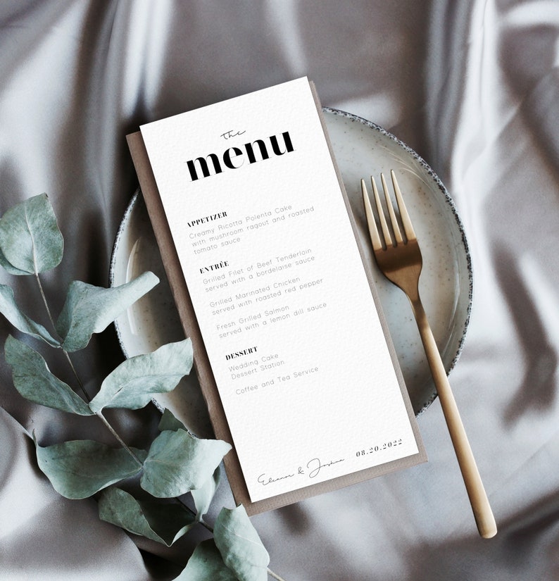 Pu&ograve; includere: Un menu bianco con testo nero che elenca gli antipasti, i piatti principali e i dessert per un ricevimento di nozze. Il menu &egrave; su un sottopiatto marrone con una forchetta dorata su una superficie beige. La data "08.20.2022" &egrave; scritta in fondo al menu.