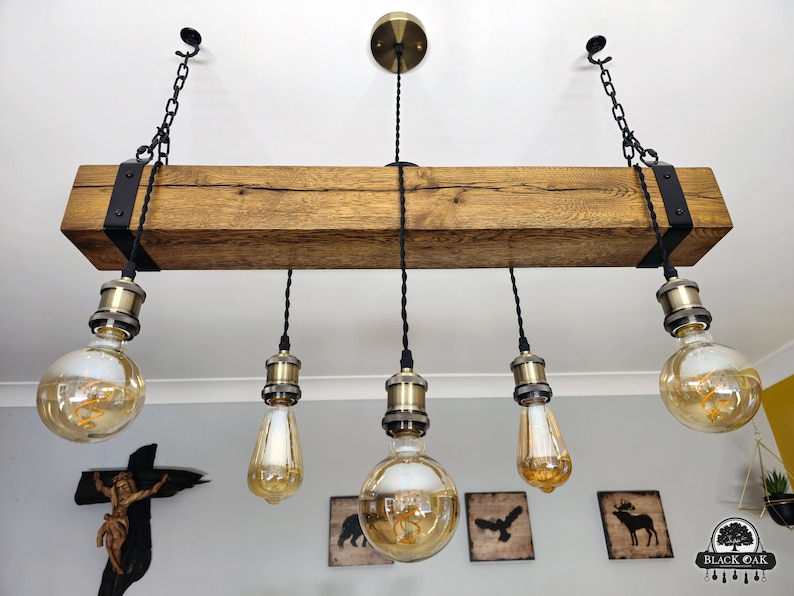 May include: A rustic wooden beam chandelier with five Edison bulb lights hanging from black cords. The beam is stained a dark brown and has black metal brackets on each end. The bulbs are clear glass with a gold finish.