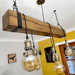 May include: A rustic wooden beam chandelier with six Edison bulb lights. The beam is dark brown with a natural wood grain and is accented with black metal brackets. The bulbs are clear glass with a warm, amber glow.