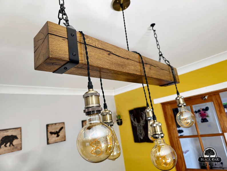May include: A rustic wooden beam chandelier with six Edison bulb lights. The beam is dark brown with a natural wood grain and is accented with black metal brackets. The bulbs are clear glass with a warm, amber glow.