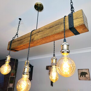 May include: A rustic wooden beam chandelier with five Edison bulb lights. The beam is dark brown with a natural wood grain and is suspended from the ceiling by black chains. The light bulbs are clear glass with a warm white glow.