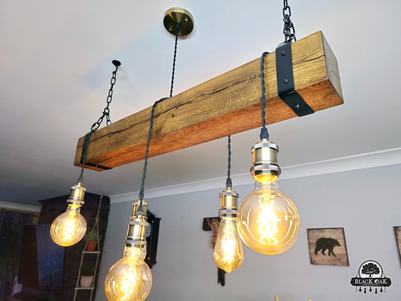 May include: A rustic wooden beam chandelier with five Edison bulb lights. The beam is dark brown with a natural wood grain and is suspended from the ceiling by black chains. The light bulbs are clear glass with a warm white glow.