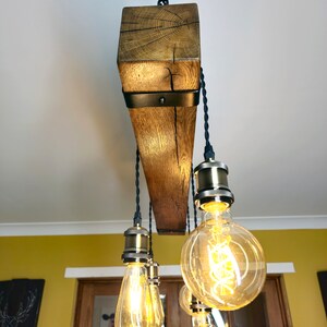 May include: A rustic wooden chandelier with six Edison bulb lights. The chandelier is made from reclaimed wood and has a black metal frame. The bulbs are hanging from black cords and have a warm, golden glow.