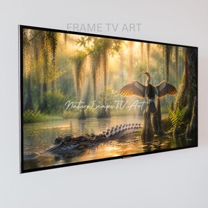 Peut inclure: Une œuvre d'art encadrée pour téléviseur présente une scène de marais sereine. Un alligator nage dans l'eau, tandis qu'un oiseau aux ailes déployées se perche sur une souche. L'image présente une végétation luxuriante, de la mousse espagnole et le texte "FRAME TV ART" et "Nature Escape TV Art".