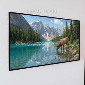 May include: A framed landscape painting of a lake scene with mountains and trees. A deer drinks from the turquoise water. The text "Nature Escape TV Art" is visible on the painting, and "FRAME TV ART" is above the frame.