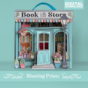 Può includere: Modello di libreria in carta nei toni del turchese, rosa e bianco, con la scritta "Book & Store" sulla tenda. Il modello presenta una facciata dettagliata con una porta, finestre e un lampione, ed è decorato con piante in vaso e cesti di fiori appesi.