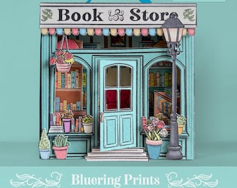 Könnte beinhalten: Ein Papiermodell eines Buchladens in Türkis, Rosa und Weiß, mit dem Text "Book & Store" auf der Markise. Das Modell hat eine detaillierte Fassade mit einer Tür, Fenstern und einer Straßenlaterne und ist mit Topfpflanzen und hängenden Blumenkörben dekoriert.