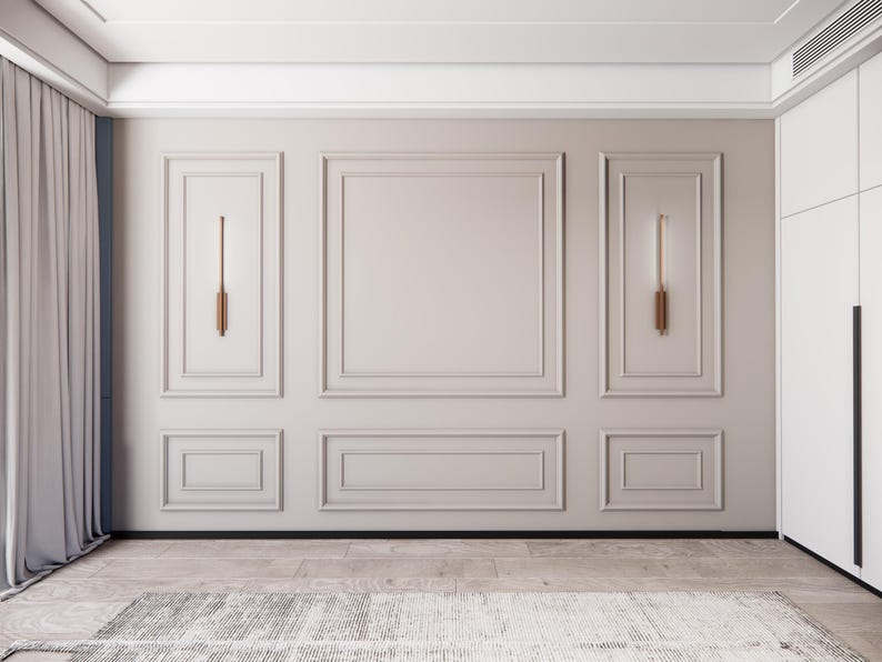Puede incluir: Una pared blanca con un dise&ntilde;o de molduras decorativas. La pared est&aacute; dividida en tres secciones con un panel rectangular en el centro. Hay dos apliques de pared, uno a cada lado del panel central. La pared est&aacute; en una habitaci&oacute;n con un techo blanco y un suelo marr&oacute;n claro.