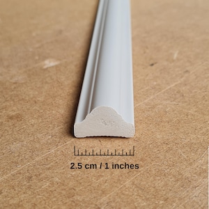 Puede incluir: Moldura decorativa blanca con un borde redondeado. La moldura tiene 1 pulgada de ancho y 2,5 cm de largo.