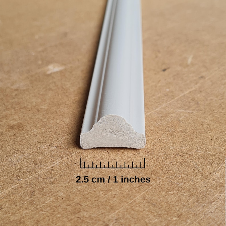 Puede incluir: Moldura decorativa blanca con un borde redondeado. La moldura tiene 1 pulgada de ancho y 2,5 cm de largo.