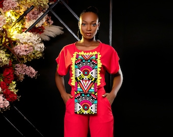 May include: A woman wearing a red jumpsuit with a black and colourful geometric pattern on the front. The jumpsuit has a short-sleeved top and wide leg trousers.