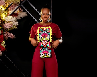 May include: A woman wearing a maroon jumpsuit with a colourful geometric pattern on the bodice. The pattern features bright colours like pink, yellow, blue, and green.