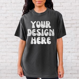 May include: A black t-shirt with a white graphic that says "YOUR DESIGN HERE" in a retro font.