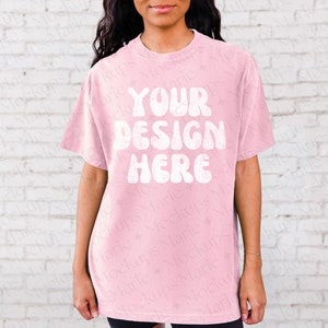 May include: A pink oversized t-shirt with the text "YOUR DESIGN HERE" in white, retro-style lettering.