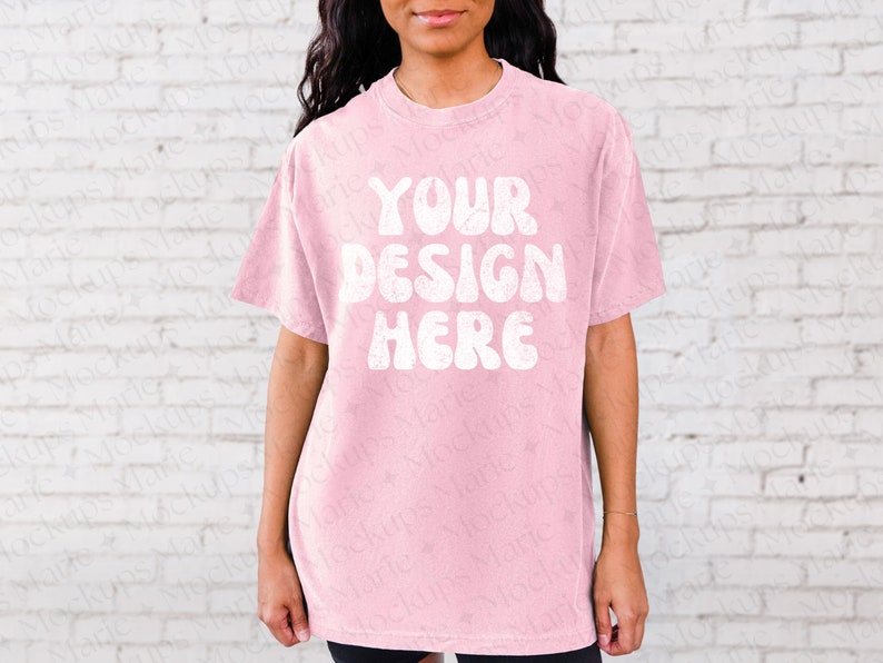 May include: A pink oversized t-shirt with the text "YOUR DESIGN HERE" in white, retro-style lettering.