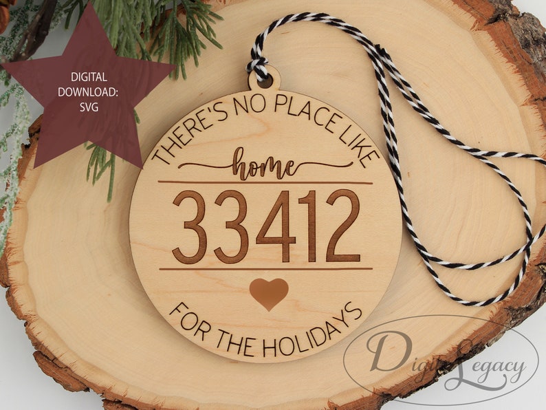 Pode incluir: Um ornamento de madeira com o texto "There's no place like home 33412 for the holidays" e um pequeno cora&ccedil;&atilde;o no centro. O ornamento est&aacute; preso a um cord&atilde;o preto e branco.