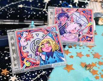 May include: Two square clear acrylic charms featuring colourful anime-style illustrations of characters in wizard hats. The front charm displays a blonde character with a blue cloak, while the back charm shows two characters with magical symbols.