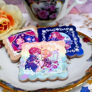 Könnte beinhalten: Drei quadratische Holzuntersetzer mit gewelltem Rand, die jeweils eine farbenfrohe Illustration im Anime-Stil zeigen. Einer zeigt ein Paar im Garten, ein anderer Charaktere in einer Theaterkulisse und der dritte eine Figur unter dem Mond.