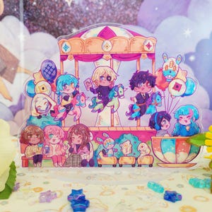 Puede incluir: Un amuleto de acrílico colorido que presenta un carrusel con personajes montando caballos, un paseo en taza de té y un grupo de personajes de pie en el suelo. El amuleto está decorado con estrellas y otros detalles caprichosos.
