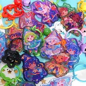 Könnte beinhalten: Eine Sammlung bunter Acryl-Schlüsselanhänger mit verschiedenen Chibi-Figuren in Zauberer- und Fantasy-Kostümen. Jeder Anhänger ist an einem sternförmigen oder runden Kunststoffring in leuchtenden Farben wie Rot, Grün und Lila befestigt.