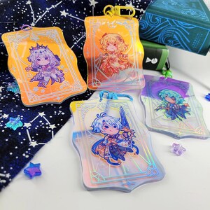 May include: Four clear acrylic keychains with anime-style illustrations. Each keychain features a different character in vibrant colors, set against a decorative background. The keychains have gold or blue clasps and are surrounded by star-shaped confetti.