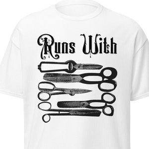 May include: White t-shirt with black text that reads "Runs With" and a graphic of a stack of vintage scissors.