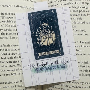 Peut inclure: Une illustration en noir et blanc d'un squelette lisant un livre sur fond de ciel étoilé. Le texte "The Late Night Reader" est en bas de l'image. L'image est un marque-page avec le texte "the bookish craft house @thebookishcrafthouse" en bas.