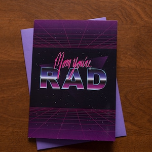 May include: A purple and black card with a retro 80s design. The card says "Mom you're RAD" in a pink and blue font.