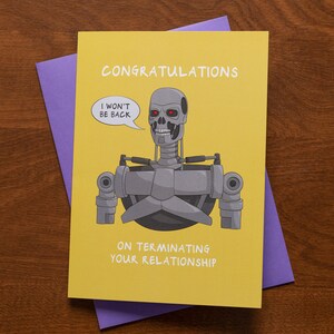May include: A yellow greeting card with the words "CONGRATULATIONS" and "ON TERMINATING YOUR RELATIONSHIP". The card features a cartoon illustration of a robot with red eyes and the phrase "I WON'T BE BACK" in a speech bubble. A purple envelope is behind the card.
