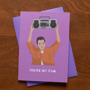 May include: A greeting card with a purple background features an illustration of a person holding a boombox above their head. The text "YOU'RE MY JAM" is written in white at the bottom of the card. A purple envelope is visible.