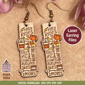 May include: Wooden laser-cut earrings with a fall theme. Each earring features a rectangular design with the words "Hay Rides, Pumpkins, Bonfires, Fall, Leaves, Autumn, Skies, S'mores" and illustrations of a pumpkin, coffee, and s'mores.