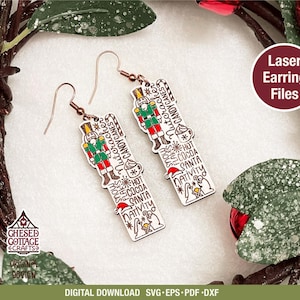 May include: A pair of Christmas-themed earrings with a festive design. Each earring features a wooden rectangular shape with a nutcracker soldier and holiday-themed text. The earrings are adorned with copper-colored ear wires and are surrounded by a decorative wreath.