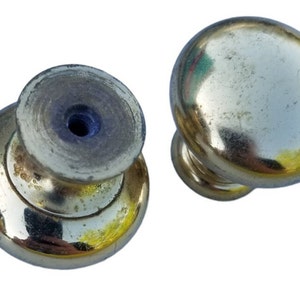 May include: Two gold-toned cabinet knobs with a round top and a smaller round base. The knobs have a smooth, shiny finish.