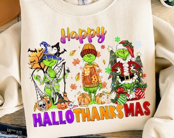 Può includere: Felpa color crema con una grafica colorata raffigurante tre personaggi del Grinch vestiti per Halloween, il Ringraziamento e Natale. Il testo "Happy HalloThanksMas" è visualizzato in colori vivaci. La felpa è abbinata a jeans blu, un cappello e sandali.