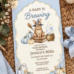 Può includere: Un invito rettangolare per baby shower con sfondo azzurro e bordo smerlato color crema. Presenta un coniglio marrone con un cappello da strega blu, seduto su libri accanto a un calderone, zucche e un fantasma con il testo A BABY IS BREWING.