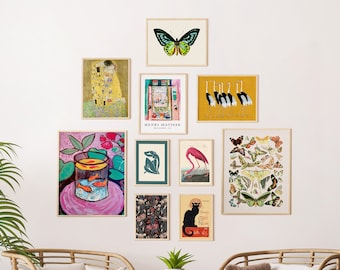 Puede incluir: Una pared de galería con una variedad de impresiones enmarcadas, incluyendo una mariposa, un flamenco, una naturaleza muerta con peces dorados y un gato negro. Las impresiones están dispuestas en un patrón simétrico en una pared blanca.